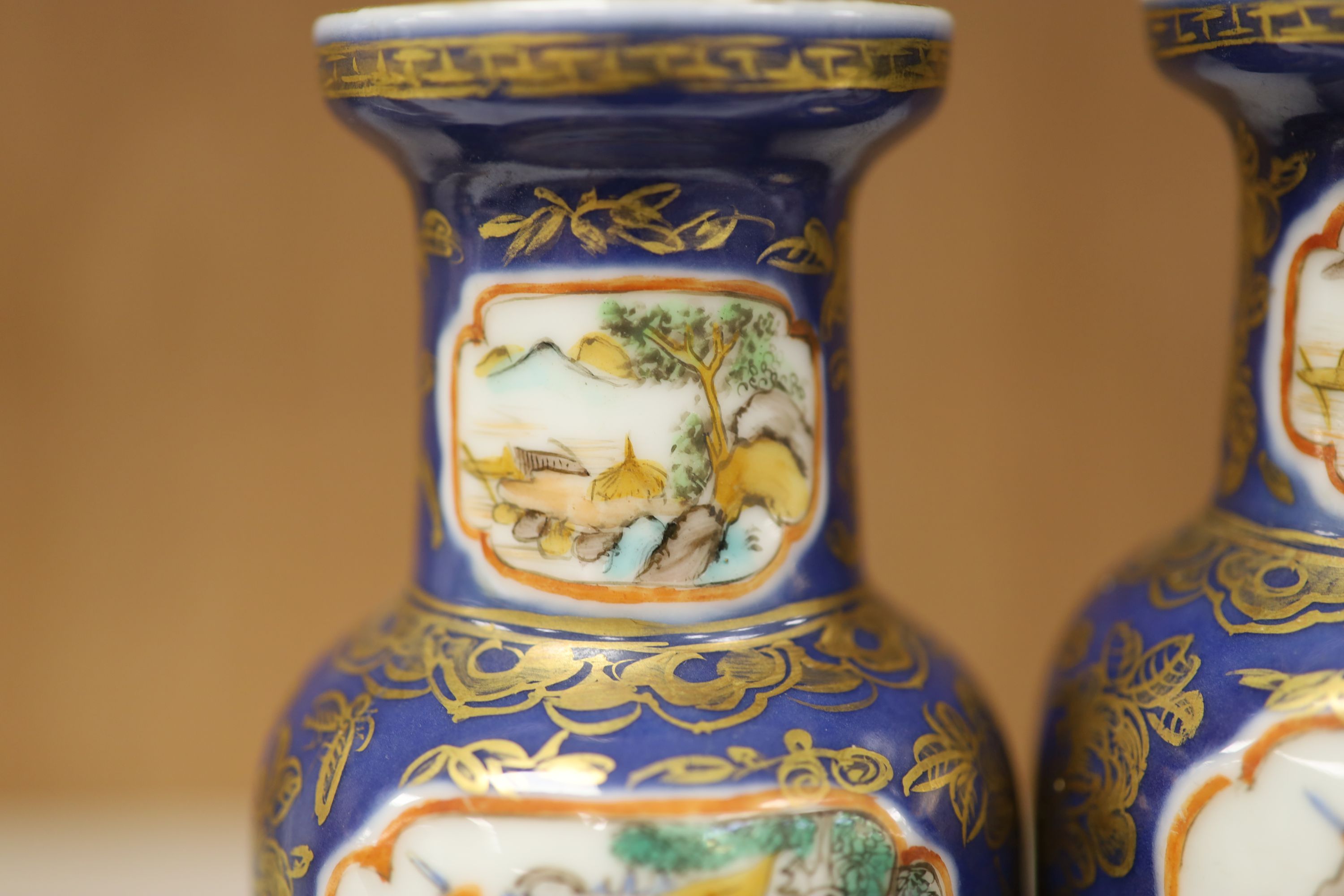 A pair of Chinese Kangxi style blue-ground vases, late 19th century decorated with panels of warriors and heightened in gilt, on carved hardwood stands, height 18cm excluding stand